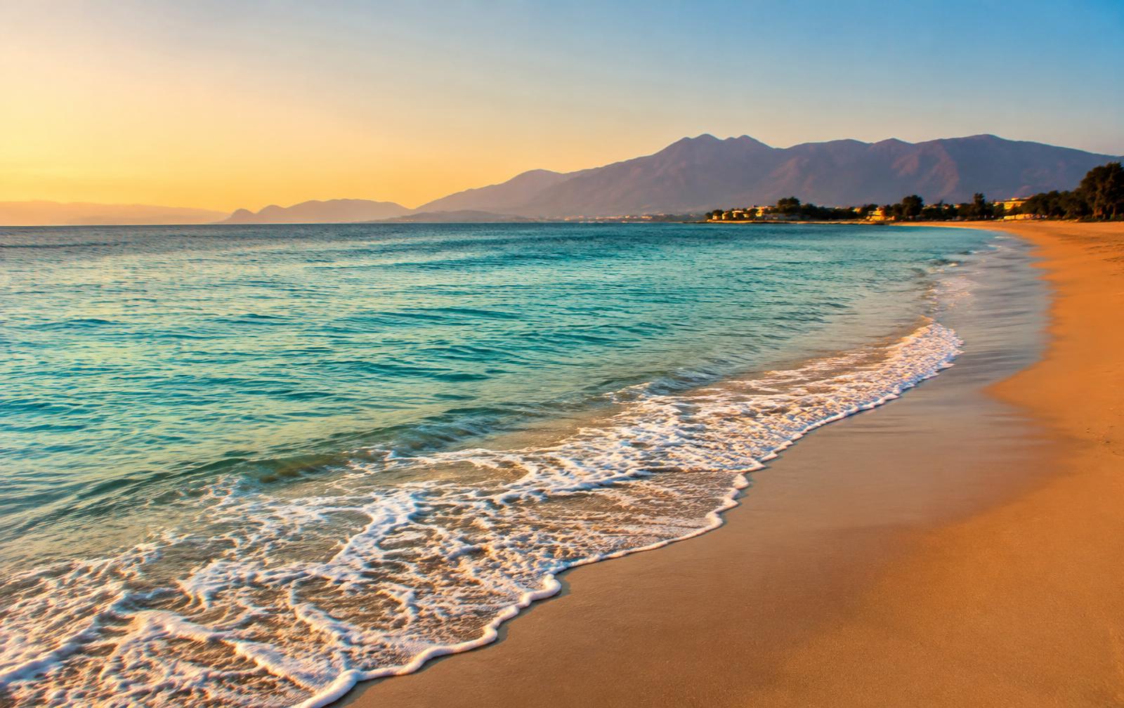 Calm turquoise sea meeting a sandy beach at golden hour with mountains beyond